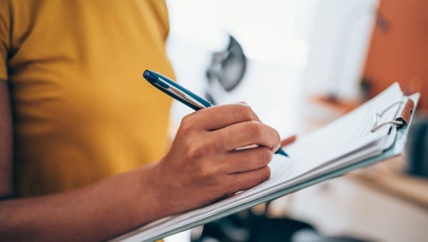 Woman hand writing on clipboard with a pen.